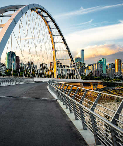 A bridge with a metal railing and a roadway is shown with a city skyline in the background at The Laurent at Laurel Apartments, Edmonton, AB, T6T 2T5