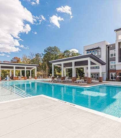 A large swimming pool in front of a building with a sunny sky above.