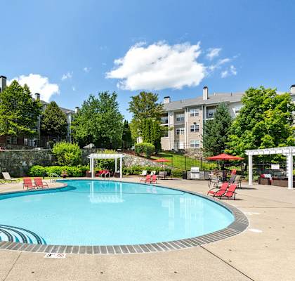 a swimming pool with red chairs and umbrellas and a building in the background