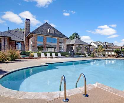 A swimming pool in front of a house with a blue sky and clouds.