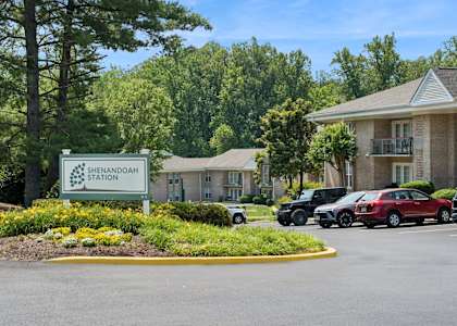 A sign for Shenandoah Station is in front of a building and some parked cars.