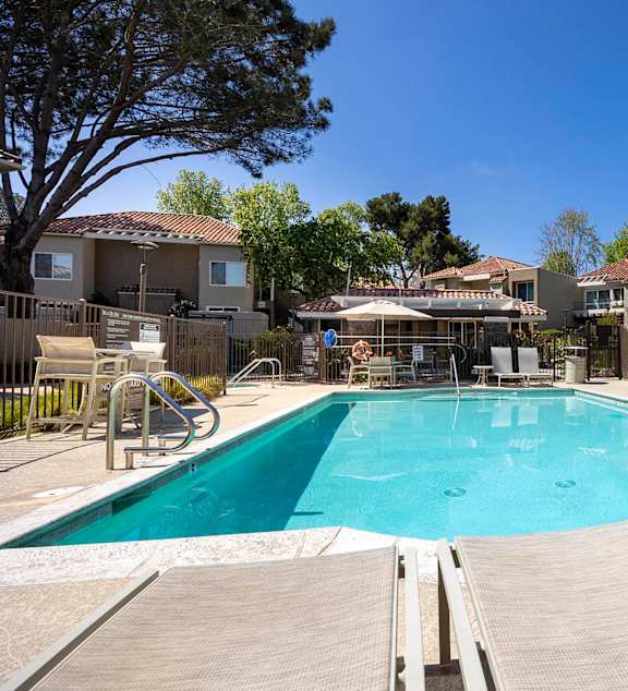 Community swimming pool with deck chairs and umbrella at Bella Del Mar Apartments, Del Mar, CA