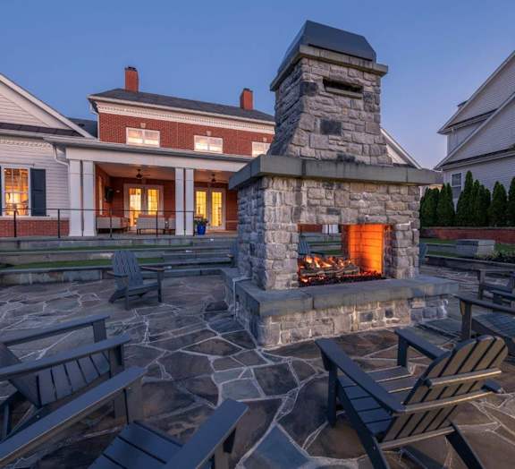 a stone fireplace in the center of a patio with chairs