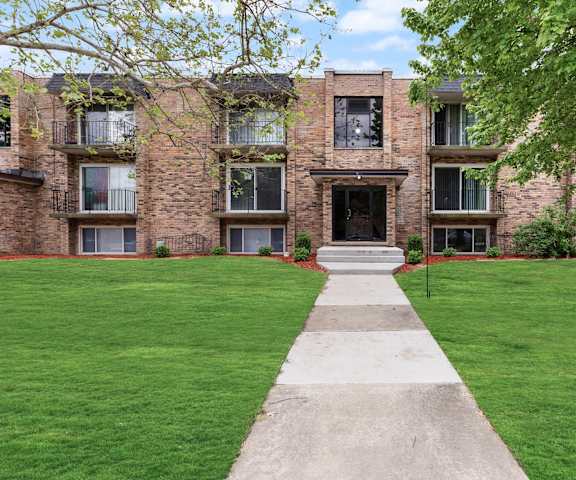 exterior view of a brick apartment building with green grass and a sidewalk