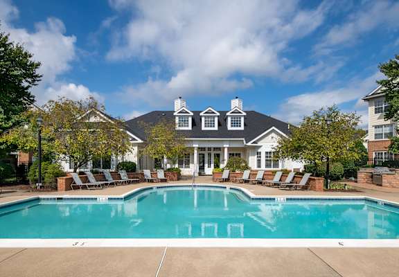 a swimming pool with chairs around it in front of a house