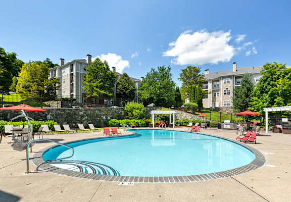 a swimming pool with red chairs and umbrellas and a building in the background