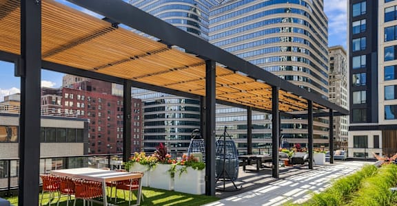 A modern outdoor seating area with a long table and chairs under a wooden canopy.