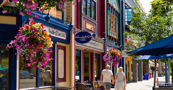 A couple walking down a street past a cafe with a sign that says "The Caffeated Cat".