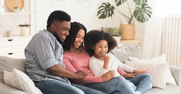 Three people are sitting on a couch, with one person holding a remote control.