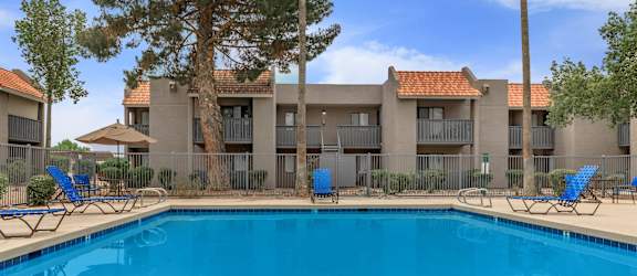 A swimming pool in front of a building with blue chairs around it.