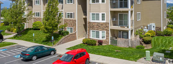 A red car is parked in front of a two-story apartment building.
