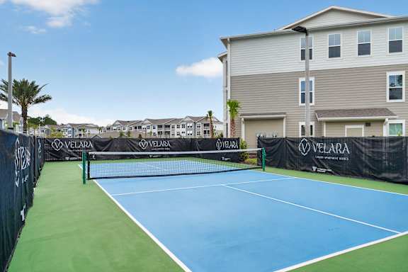 A tennis court is surrounded by apartment buildings.