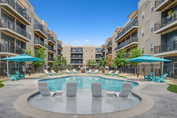 a swimming pool with lounge chairs and umbrellas in the center of the vue apartments in indianapolis