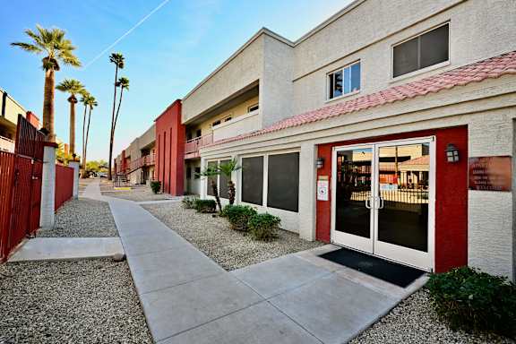 A building with a red door and windows is surrounded by palm trees.
