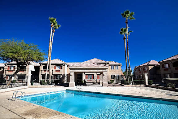 A swimming pool in front of a building with palm trees.