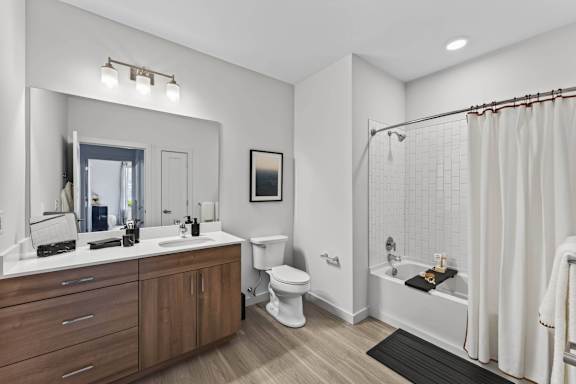 Apartment bathroom with a double vanity, toilet, soaking tub, and subway tile surround.