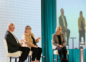 Thumbnail 14 of 21 - Three people are sitting on stage in front of a screen with another person on it.