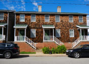Thumbnail 1 of 2 - a red brick apartment building with cars parked in front