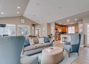 Thumbnail 2 of 6 - A living room with a grey couch, a blue armchair, and a coffee table.