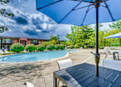 Thumbnail 1 of 5 - A blue umbrella is over a table in front of a pool.