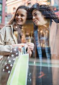 Two women are standing outside a store, one holding a shopping bag.