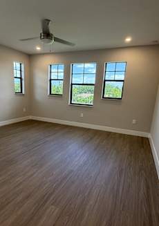 A room with a ceiling fan and three windows.