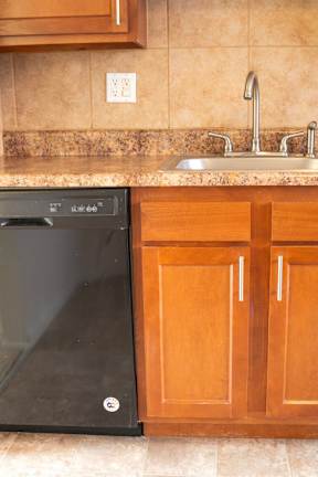 A black dishwasher is in a kitchen with wooden cabinets.