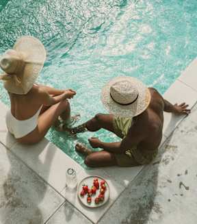 Two people sitting by a pool with a plate of food in front of them.