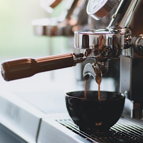 A coffee machine is dispensing coffee into a black cup.