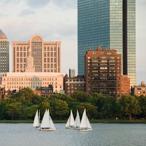 Three sailboats are sailing on a body of water in front of a city skyline.