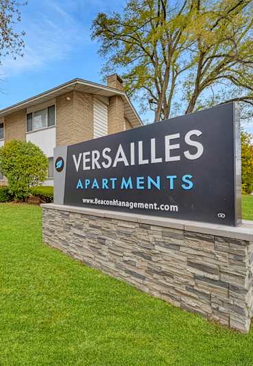 A stone wall with a sign that says Versailles Apartments.