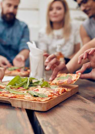 A group of people are gathered around a wooden table, enjoying a pizza and beer together at The Laurent at Laurel Apartments, Edmonton, AB, T6T 2T5