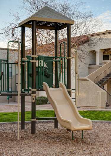A basketball court with a bench on the side and two houses in the background.