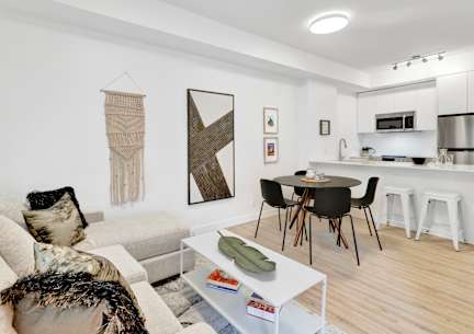 A modern living room with a white sofa, a coffee table, and a dining area in the background.