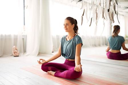 A woman is sitting cross-legged on a yoga mat in a room.