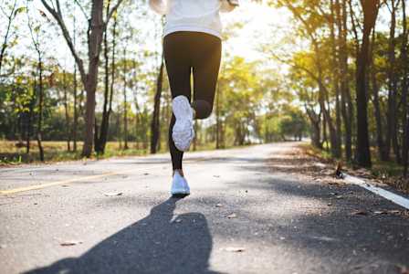 A person is running on a road with trees on both sides.