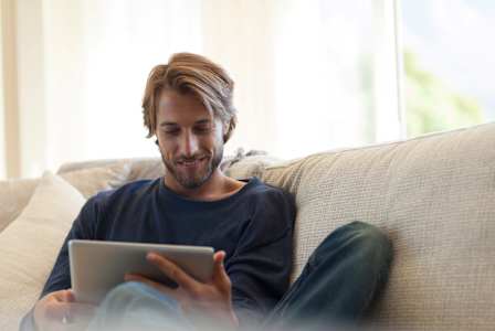 A man is sitting on a couch using a tablet.