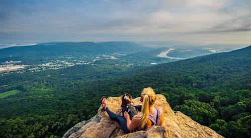 two women sitting on a rock looking at the view of a river