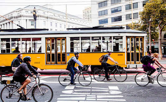 A yellow tram is on a street with people riding bikes in front of it.at The Rise, San Francisco, 94103