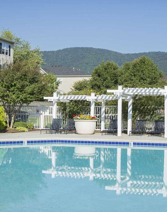 A pool with a white pergola and chairs around it.