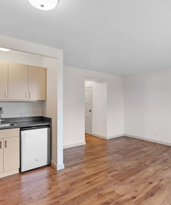 an empty living room with a kitchen with a stove and refrigerator