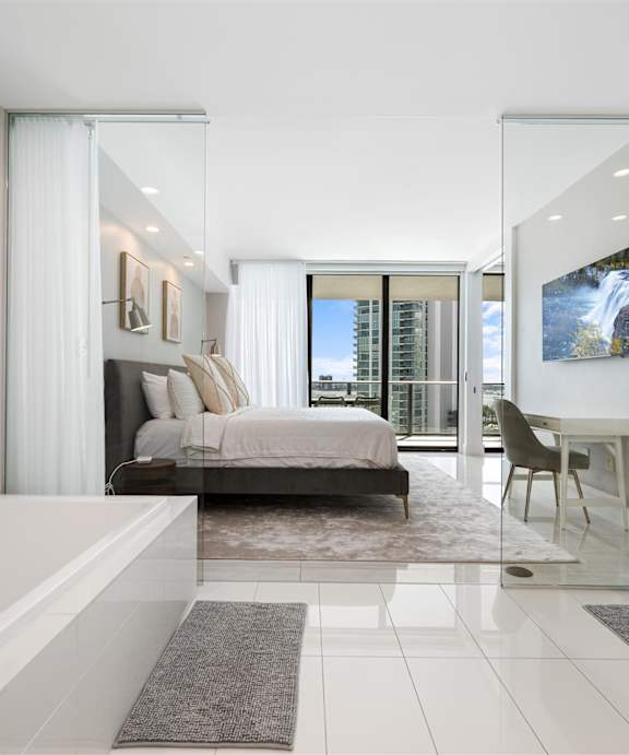 A white bedroom with a bed, nightstand, and a television.