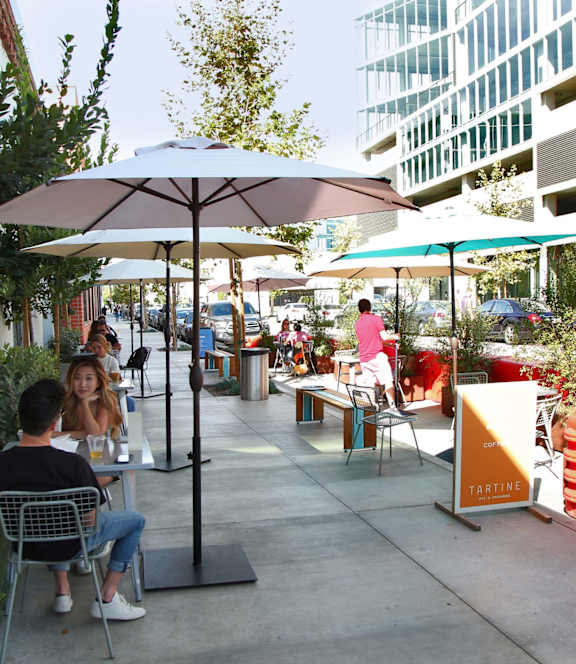 A man and woman are sitting at a table under an umbrella in a courtyard.
