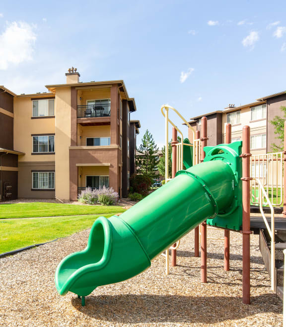 a green slide in the middle of a grassy area in front of an apartment complex