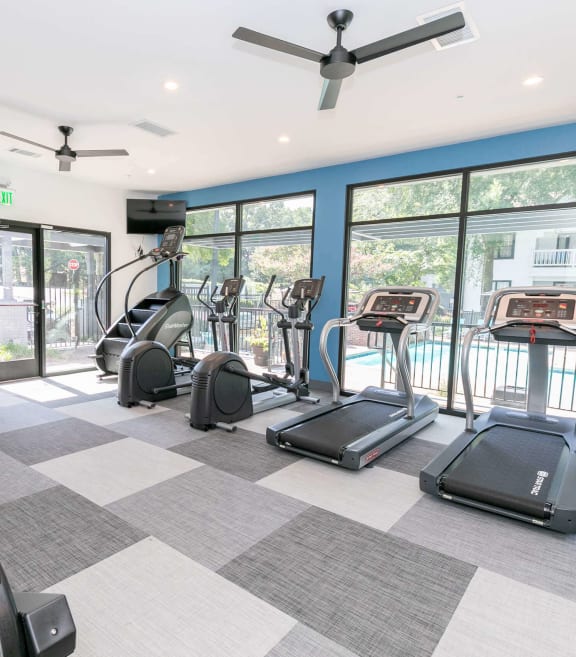 the gym is equipped with cardio equipment and glass windows