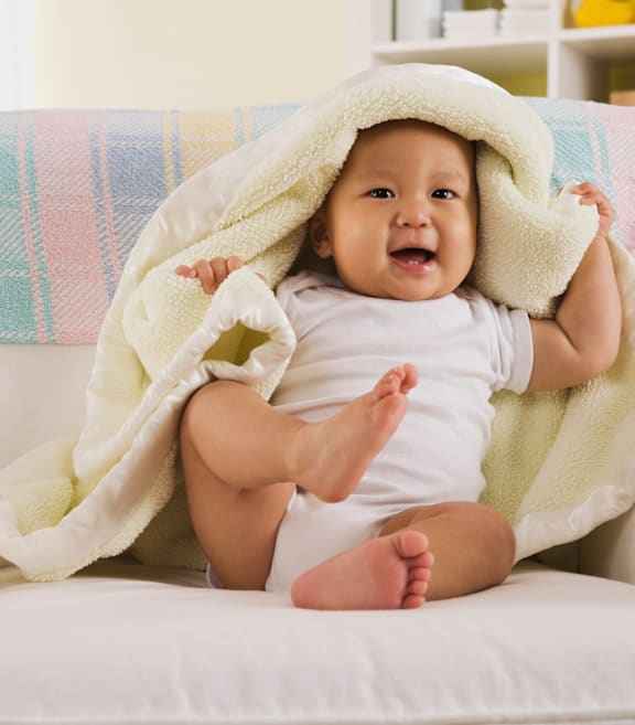 A baby is sitting on a couch under a colorful blanket.at Northside Hills Apartments, Georgia