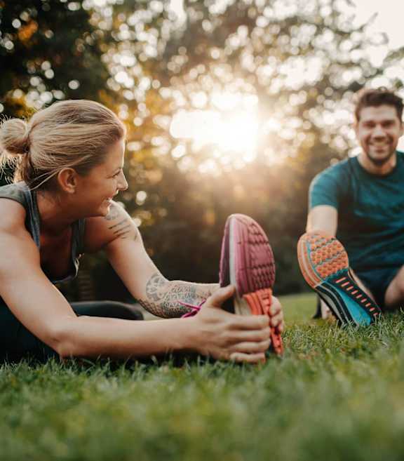 A man and a woman are sitting on the grass, stretching their legs.