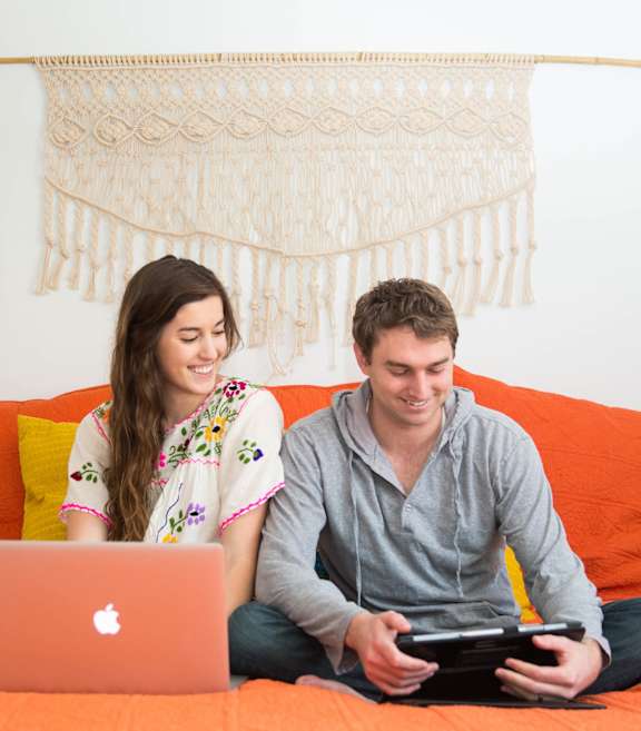 A man and a woman are sitting on a bed with a laptop and a tablet respectively. at Stratford at Southern Towers, Alexandria, 22311