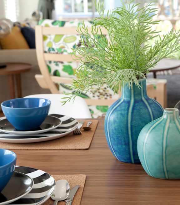 A dining table with blue bowls, plates and vases.