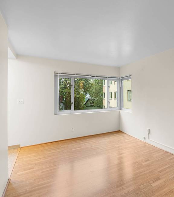 a living room with white walls and a window and wood floors